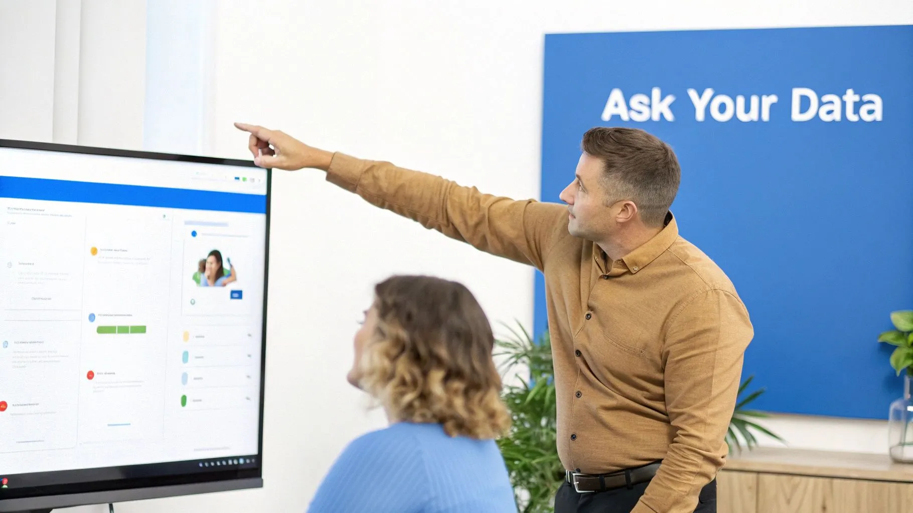 Two business professionals analyzing data on a large screen in an office with an 'Ask Your Data' sign.